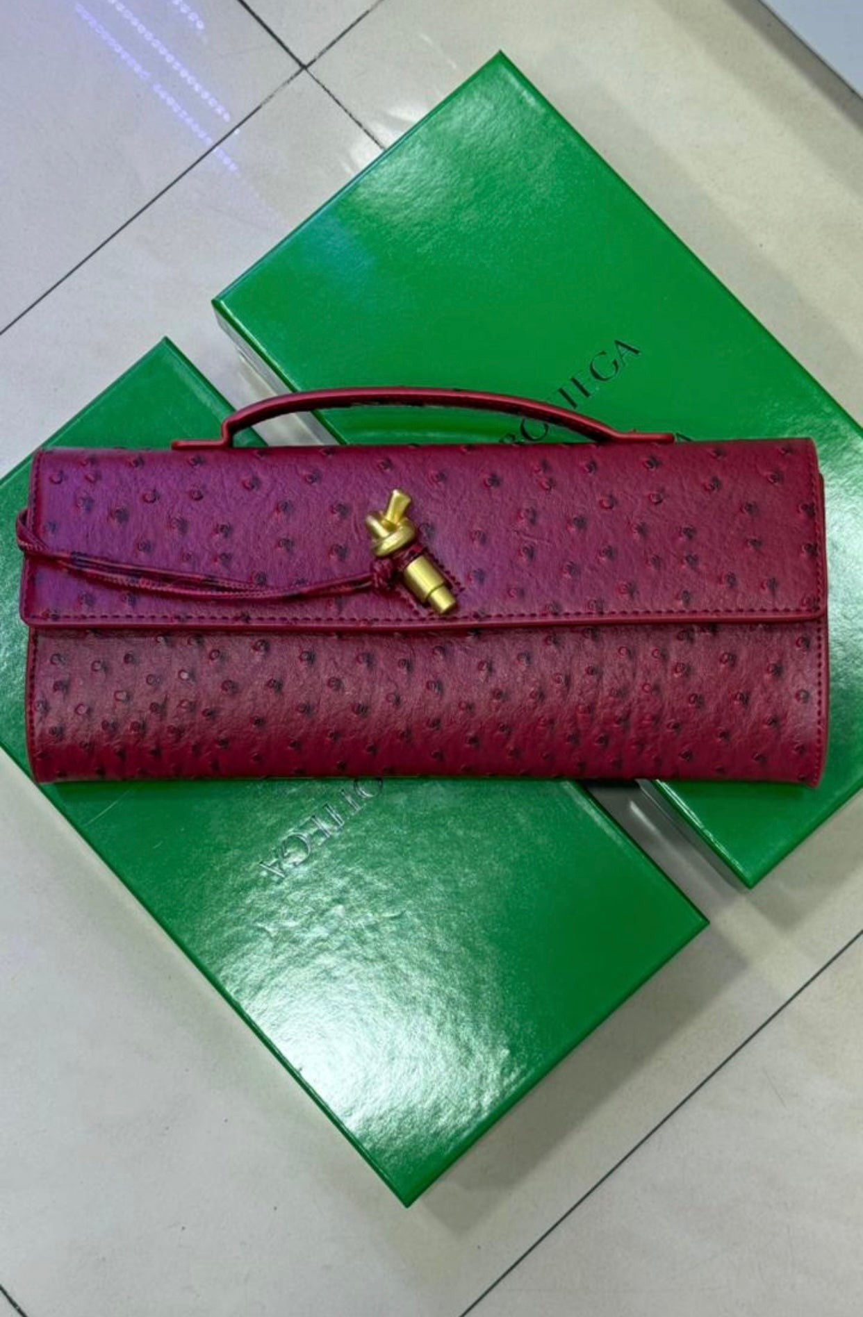 Pochette à anse en autruche avec fermeture knot emblématique en métal.
