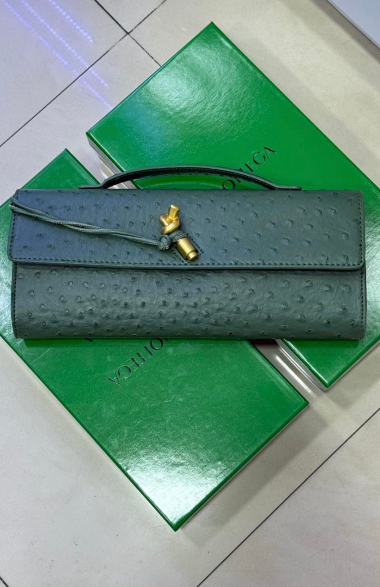 Pochette à anse en autruche avec fermeture knot signature.